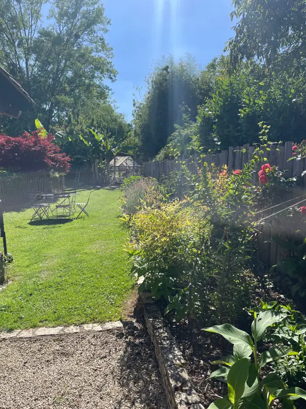 Une allée de pelouse bordée de massifs fleuris, avec une table et des chaises au soleil.