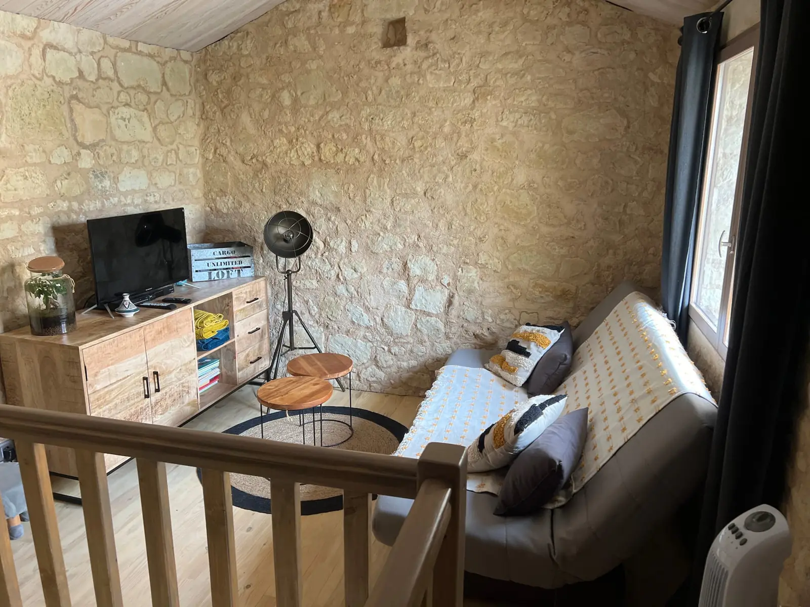 La mezzanine aux murs en pierre, avec le canapé-lit, un meuble en bois et la télévision.